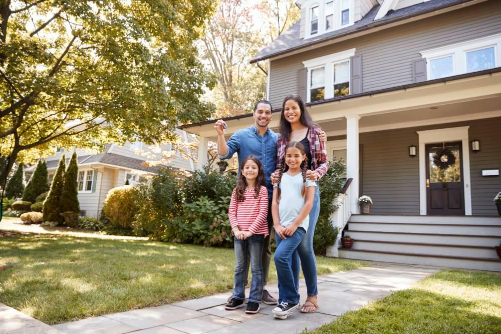 Young family holding keys in front of house.